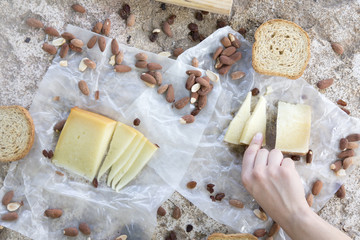 Woman hand holding a piece of cheese of snack of cheese, roasted bread and almonds