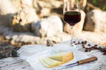 Pieces of cheese and raisins with a red wine glass on a old wood table
