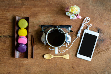 Colorful macaroons and a cup of coffee with cellphone on wooden