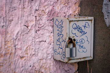 old grey rusty padlock on grey metal grey graffiti box on pink wall
