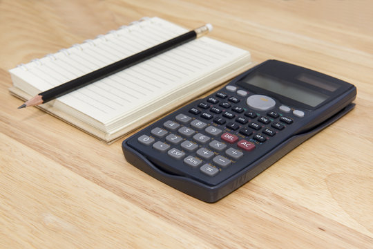 calculator, note and pencil on wood background