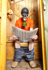 Man in respirator reading newspaper in wooden village WC - obrazy, fototapety, plakaty