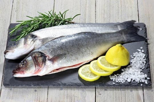 k&uuml;chenfertig ausgenommene Wolfsbarsche auf Schieferplatte mit Rosmarin, Zitrone und Meersalz