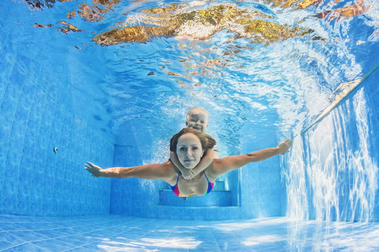 Happy family - positive mother with baby girl swimming and diving underwater with fun in outdoor pool. Healthy lifestyle, active parents, and people water sports activity on summer holidays with child