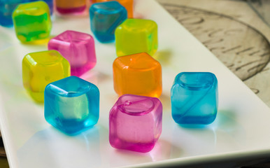 horizontal image of colourful plastic water filled ice cubes sitting on a white plate.
