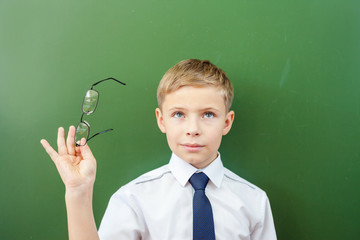 Happy schoolboy standing near the blackboard with medical glasses
