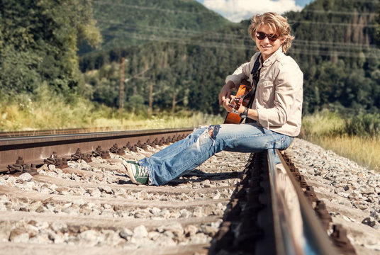 Happy smiling young man with guitar sitting on railway