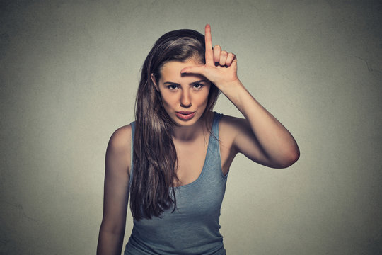 young unhappy woman giving loser sign on forehead