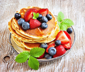 Stack of pancakes with berries and maple syrup for breakfast, sective focus