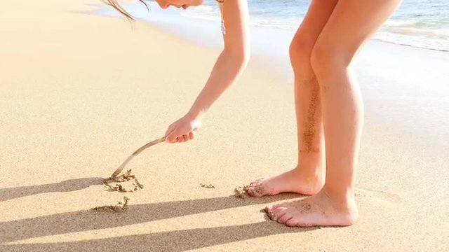 Cute blonde girl writing in sand on a beach