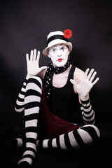 Fototapeta na wymiar Theatrical mime with red flower sits on the floor
