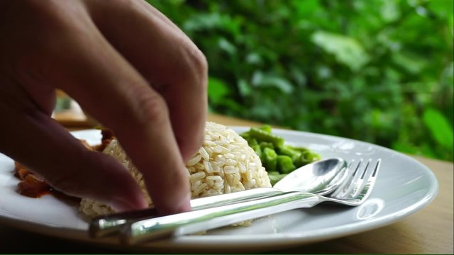 Human hands eating brown rice with spoon and fork