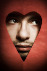 Face of young man peering from hole in heart-shaped