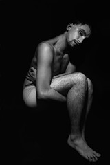 young naked man in his underwear lying on a black background