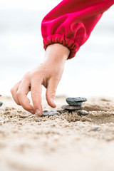 Little Hand placing Stone on the Pyramid on sand. Sea in the bac