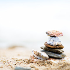 Fototapeta na wymiar Stones pyramid on sand. Sea in the background