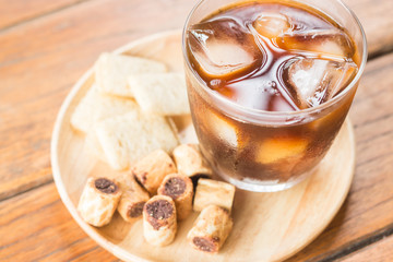 Glass of black iced coffee with some snack