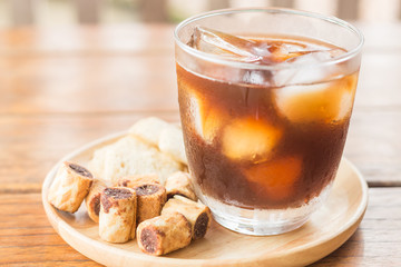Glass of black iced coffee with some snack