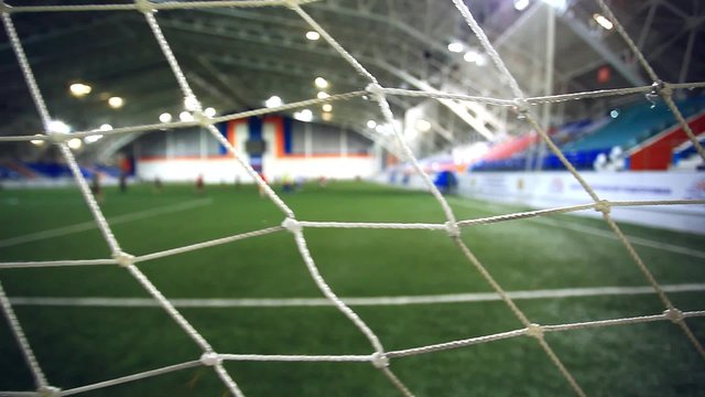 view through focused net. Blurred players play on Soccer field