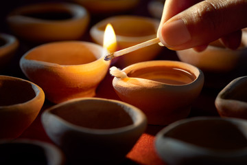 Hand holding a matchstick lighting diya lamps during diwali celebration