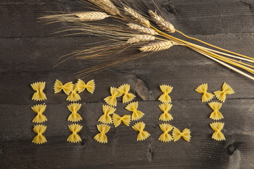 farfalle di pasta compongono scritta Italy disposte su  ripiano di legno con spighe di grano
