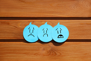 Sad emotions on blue stickers on wooden background. Group of negative emotions