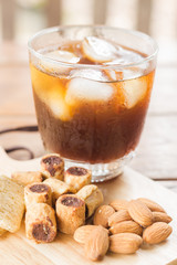 Glass of black iced coffee with some snack