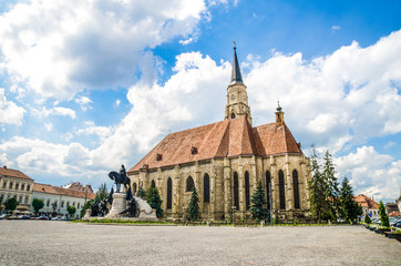 Cluj Napoca Unirii Square with the medieval gothic St Michael Church and the statue of Matei Corvin or Matias Rex on a sunny summer day with a beautiful sky in Transylvania region of Romania