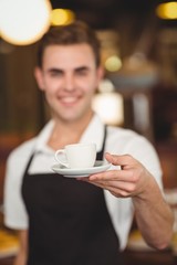 Smiling barista offering cup of coffee to camera