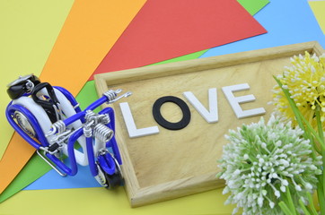white word and black O on colourfull background.green, yellow and white artificial flower placed on right.wired handcraft scooter with blue color placed on left