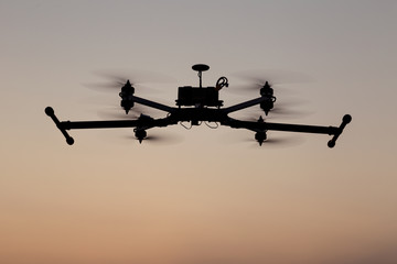 Quadcopter drone flying on sunset sky