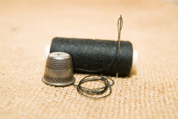 Needle, thimble and thread spool on the old cloth