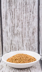 Fenugreek seeds in white bowl over wooden background