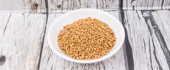 Fenugreek seeds in white bowl over wooden background