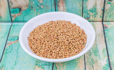 Fenugreek seeds in white bowl over wooden background
