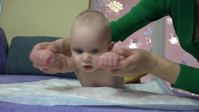 Tender woman carefully exercise little baby boy son hands on bed at home. Woman care newborn health. 4K UHD video clip.
