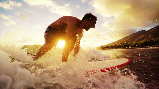 Young Man Surfing a Longboard Through a Golden Sunset in Hawaii. Warm Tone.