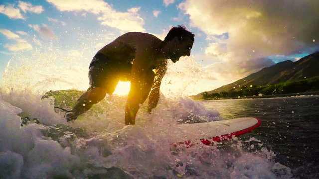 Young Man Surfing a Longboard Through a Golden Sunset in Hawaii