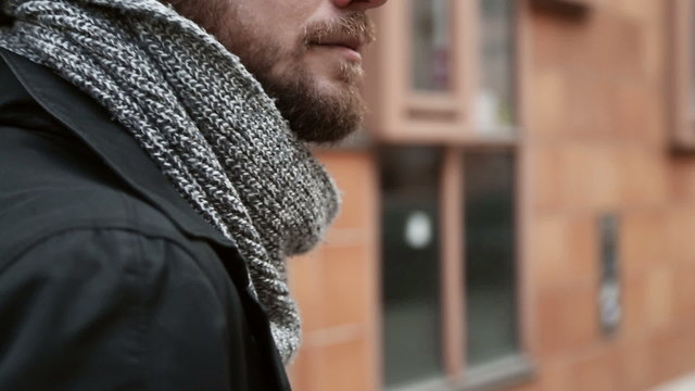 Young man in his 20s walking in a city wearing a black jacket and scarf