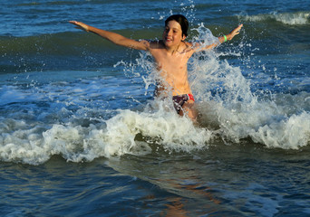 young boy makes SPLASHING in the waves of the sea in summer