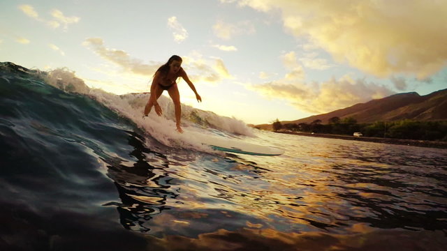 Young Attractive Girl Surfs Towards the Camera on a Longboard during a Golden Sunset in Hawaii. 