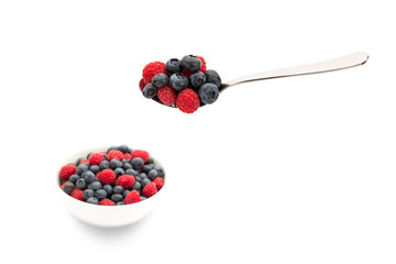 Blueberries and raspberries on a spoon with a filled bowl in background blur.
