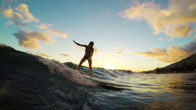 Young Attractive Girl Surfs a Longboard Through a Golden Sunset. View from in the Water in Slow Motion
