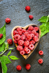 Fresh raspberries with leaves in a bowl in the shape of a heart