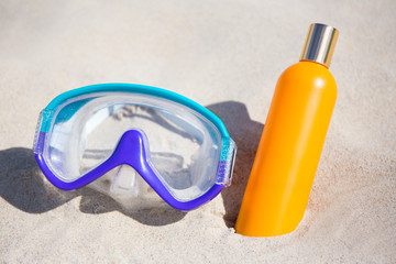 diving mask and suntan lotion bottle on sandy beach