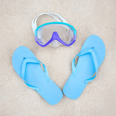 Fototapeta na wymiar beach concept - blue flip flops and diving mask on the sand