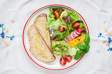 Plate with bread, smashed avocado and fresh vegetables