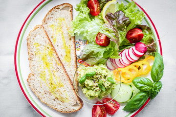 Plate with bread, smashed avocado and fresh vegetables