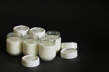 Obraz na płótnie Canvas Шесть стеклянных баночек с молоком и белые крышки на черном фоне