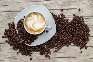 Cappuccino in weißer Tasse auf Holzuntergrund mit Kaffeebohnen